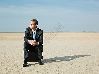 商人坐在沙漠里的公文包上图片