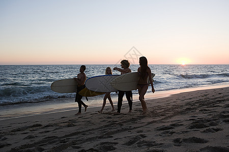 日落时分沿着海滩散步的冲浪者图片