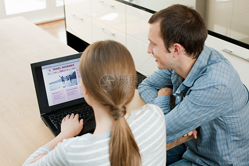在笔记本电脑上看旅行保险的年轻夫妇图片