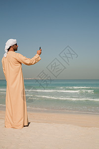 在海滩上使用手机的中东男人图片
