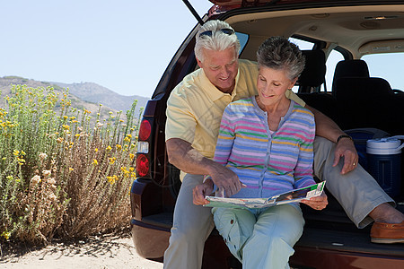 一对成熟的情侣坐在带地图的汽车后备箱上图片
