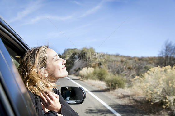 年轻女子从车窗探出头的侧视图闭上眼睛微笑图片