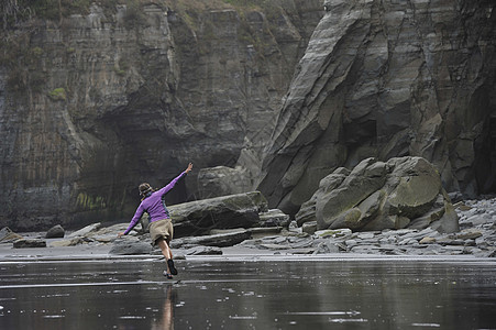 新西兰北岛海滩上张开双臂奔跑的年轻女子图片