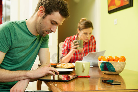 年轻夫妇吃早餐时男人用数字平板电脑图片