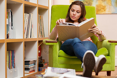 坐在绿色扶手椅上看书的年轻女子图片