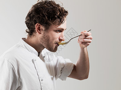 厨师在白色背景下用勺子品尝食物背景图片