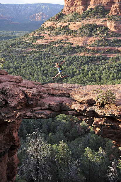 美国亚利桑那州塞多纳拱形岩层上的女性徒步旅行者在空中跳跃图片