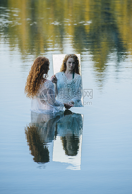 年轻女子站在湖中拿着镜子看着镜子里的倒影图片