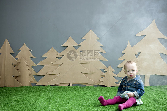 小女孩坐在草地上背景是纸板森林图片