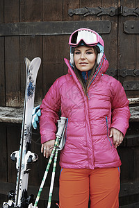 年轻女子靠在门上穿着滑雪服拿着携带滑雪器材图片