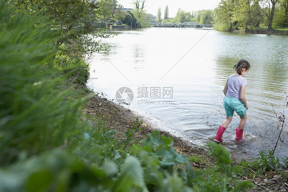 穿雨靴的女孩在池塘边涉水图片