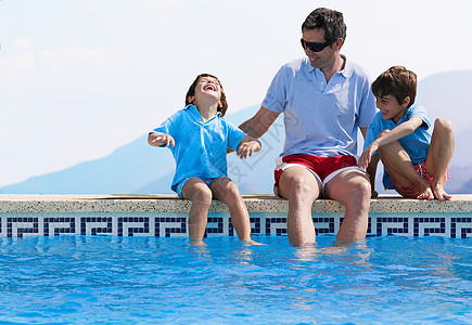 父亲和孩子坐在游泳池旁图片