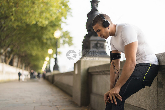 戴着耳机在河边休息的年轻男性跑步者图片