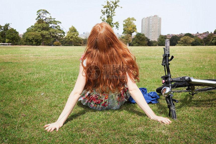 在自行车旁边的草地上休息的女人图片