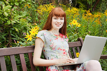 在公园长椅上操作笔记本电脑的女人图片