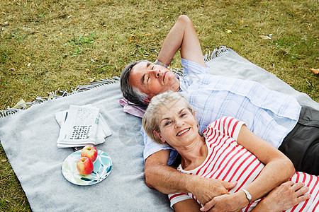 草地上的女人一对夫妇躺在草地上的野餐毯上背景