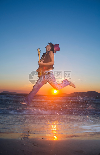 日落时分，年轻人拿着吉他跳起来图片