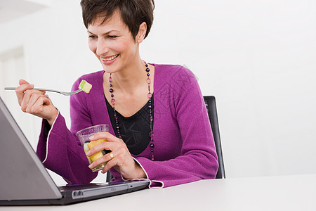 在电脑前吃水果的女人图片