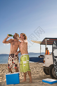海滩上的年轻人在吉普车旁喝啤酒图片