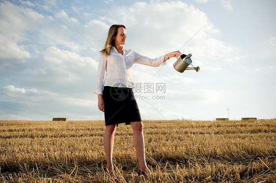 女人把水倒在麦田上图片