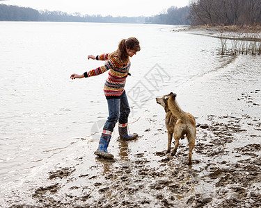 在河边和狗玩耍的年轻女人背景