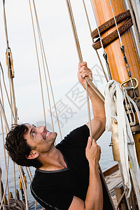 坐在帆船甲板上拉绳的男人图片