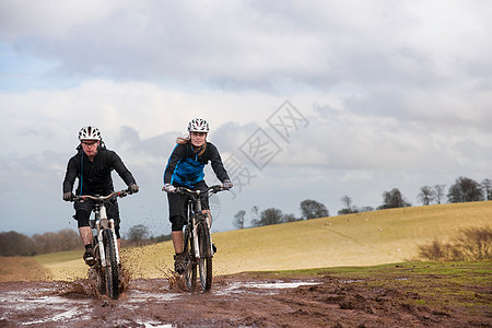 山地越野一对夫妇骑自行车穿过泥泞的水坑背景