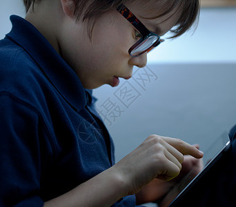 在数字平板电脑上使用触摸屏的戴眼镜男孩的特写镜头背景图片
