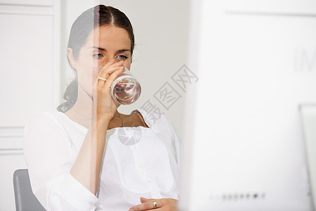 坐在电脑桌旁喝水的女人图片
