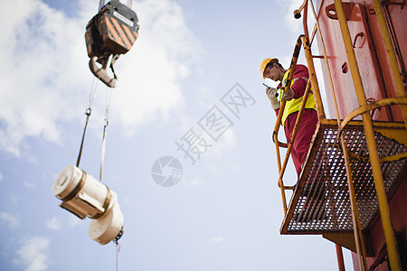 在石油钻机上指挥起重机的工人图片