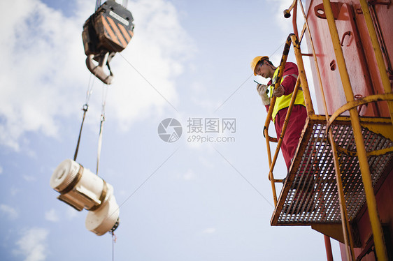 在石油钻机上指挥起重机的工人图片