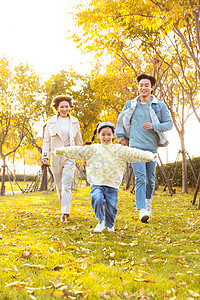 幸福的一家三口爸爸妈妈带着女儿在公园草地奔跑背景
