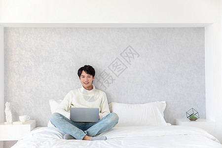 青年男性坐在床上使用电脑图片