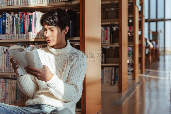 青年男性倚靠在书架上看书图片