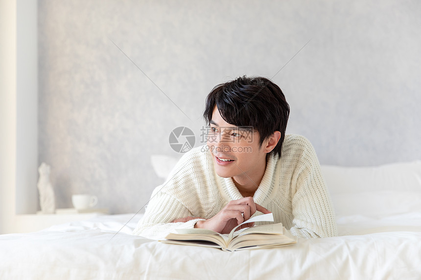 居家男性躺在床上看书图片