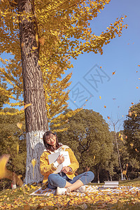 金色叶子倚靠在银杏树下看书的女孩背景