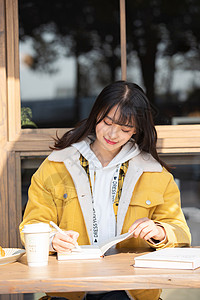 边喝咖啡边阅读坐在咖啡厅学习的女大学生背景