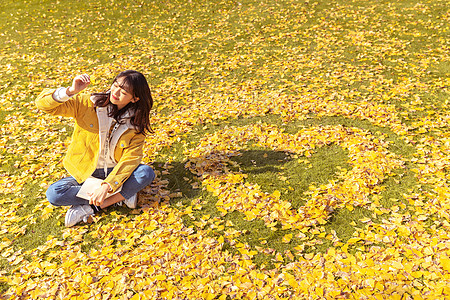 立秋坐在铺满银杏叶的草坪上看书的女孩背景