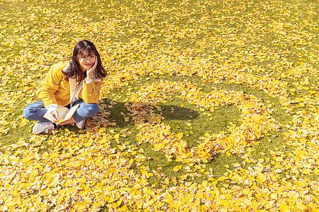 爱心与圆坐在铺满银杏叶的草坪上看书的女孩背景