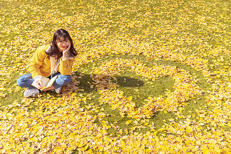 坐在铺满银杏叶的草坪上看书的女孩图片