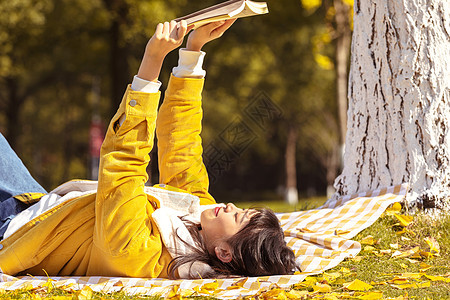 躺在铺满银杏叶的毯子上看书的女孩图片