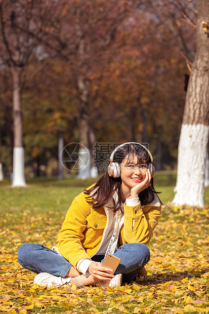 坐在铺满银杏叶的草坪上听音乐的女孩图片