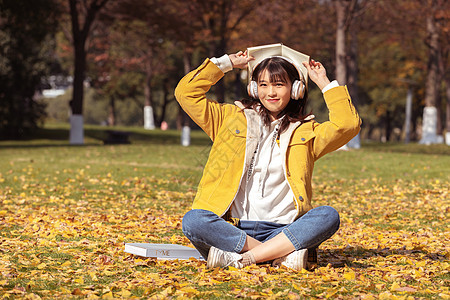 坐在铺满银杏叶的草坪上听音乐的女孩图片