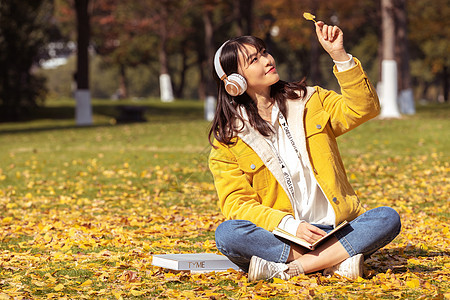 坐在铺满银杏叶的草坪上听音乐的女孩图片