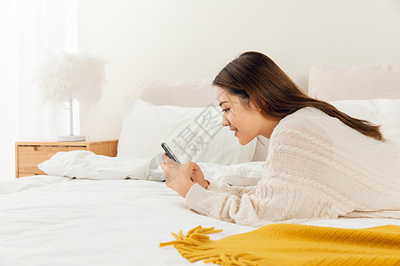 女性趴在床上玩手机聊天高清图片