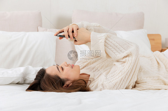 年轻女性躺床上看手机图片