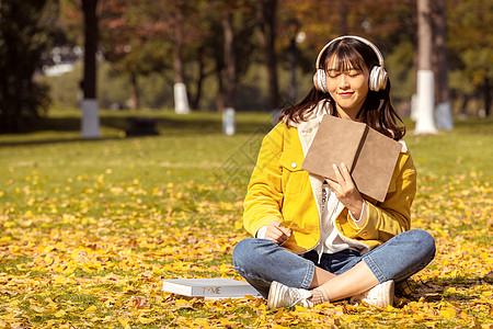 金色耳机坐在满地银杏叶下听音乐的女孩背景