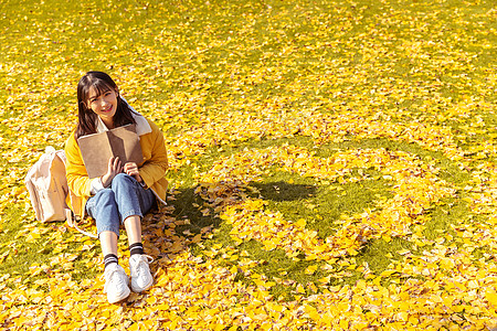 红辣椒图形坐在铺满银杏叶的草坪上看书的女孩背景