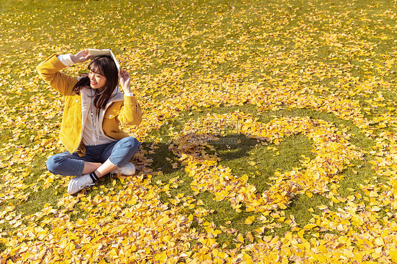 坐在铺满银杏叶的草坪上看书的女孩 图片