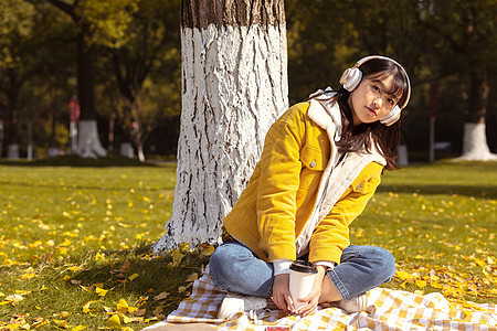 坐在铺满银杏叶的毯子上听音乐的女孩图片